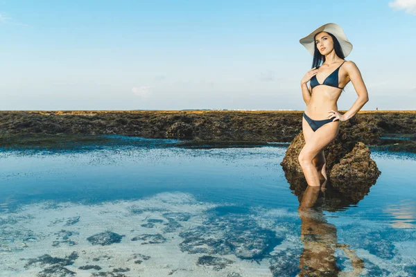夏休暇幸福屈託のない陽気な女熱帯浜の行先を楽しんで水に立っています。休暇海水に麦わら帽子を持って後ろからリラックスした休日のビキニの女の子. — ストック写真