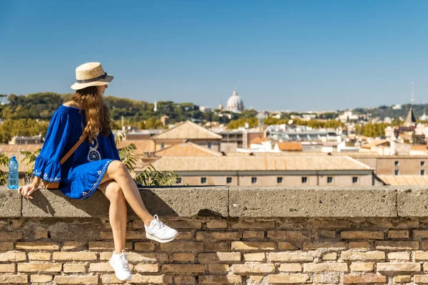 Krásná žena v modrých šatech a bílý klobouk sedí na vyhlídkové palubě s panoramatickým výhledem na Řím, Itálie — Stock fotografie