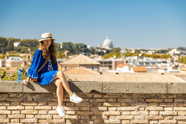 Mulher bonita em vestido azul e chapéu branco sentado no convés de observação com uma vista panorâmica da Roma, Itália — Fotografia de Stock