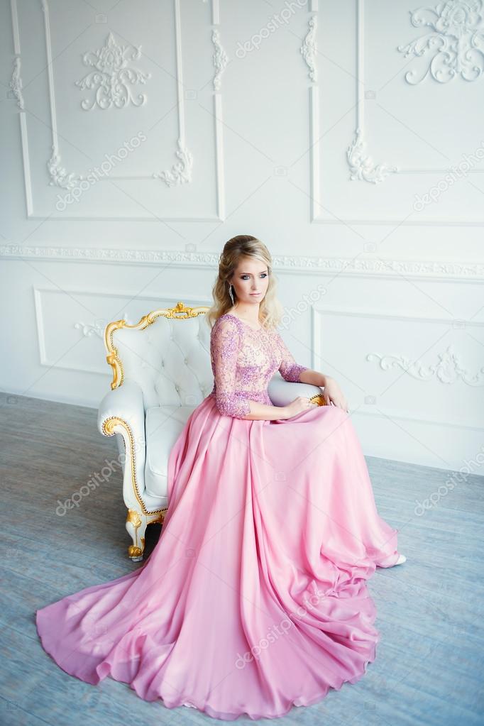 Beautiful blonde woman in evening pink dress. Classic white interior.
