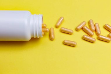 Sarı arka planda beyaz bir kavanoza saçılmış turuncu haplar..