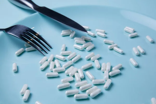 pills on plate with fork and knife on blue background