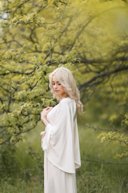 Çekici genç sarışın kadın arka planda yeşil ağaçlarla parkta eğleniyor..