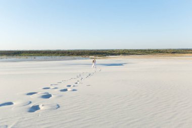 Yeni evliler, beyaz çölde kumların üzerinde yalınayak yürürler. Çölde aşk, yeni evliler..