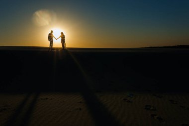 Yeni evliler gün batımında beyaz çölde çıplak ayakla yürür..