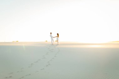 Yeni evliler gün batımında beyaz çölde çıplak ayakla yürür..