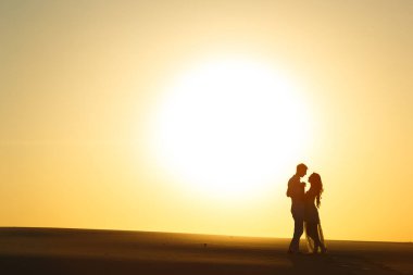 Yeni evliler gün batımında beyaz çölde çıplak ayakla yürür..