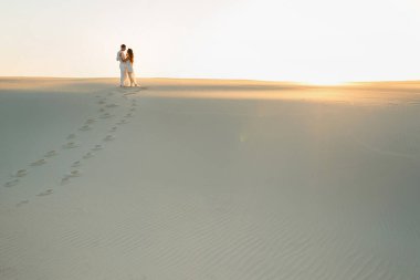 Yeni evliler gün batımında beyaz çölde çıplak ayakla yürür..