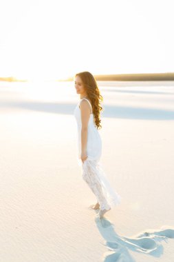 Zarif, klasik tarzda bir elbise giymiş güzel bir kız yaz tatili boyunca Maldivler 'in beyaz kumlarında yürür, ışıl ışıl, pozitif duygular içinde gülümser..