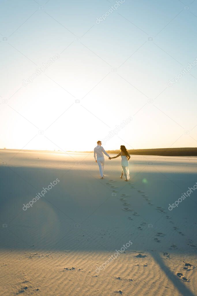 Newlyweds walk barefoot on the sand in the white desert at sunset.