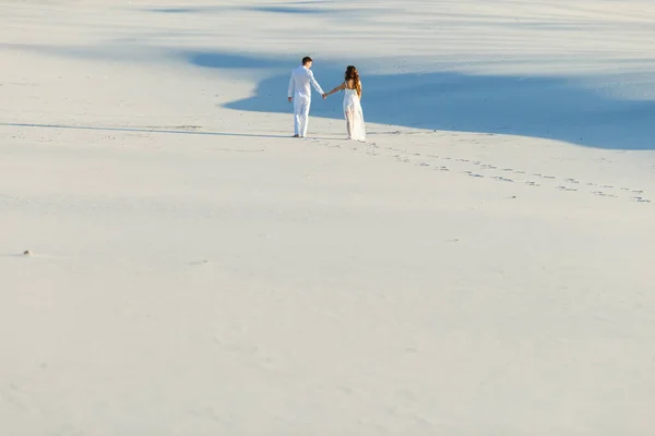 Lovers walk barefoot on the sand in the white desert. Love in the desert newlyweds.