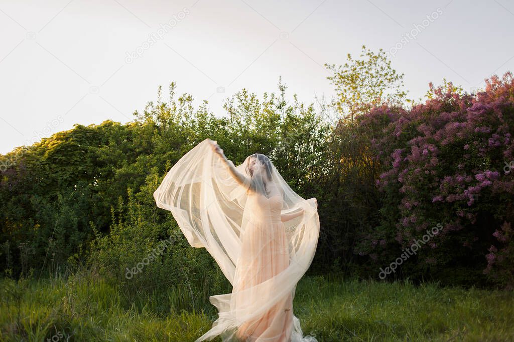 Portrait of a beautiful young brunette bride woman in a dress and with a long veil Curling in the wind on the nature garden in the summer. Fine art, wedding.