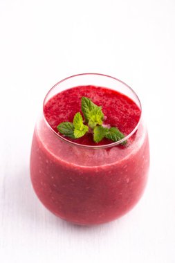 Beyaz taş masada bir bardak çilekli ve ahudududulu smoothie, sağlıklı kahvaltı içeceği.