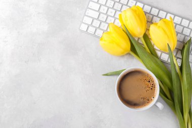 Sarı laleler kahve fincanı ve klavye gri taş masada, üst manzara düz.