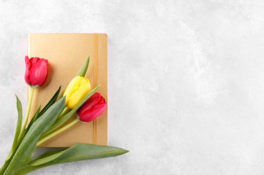 Sarı ve kırmızı laleler, gri taş masanın üzerinde altın not defteri, en üstteki düz görünüm, kopyalama alanı.