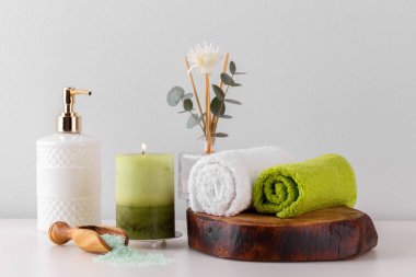 Sağlık hizmetleri ve spa malzemeleri beyaz rafta, yeşil havlular mum sabun ve tuz.