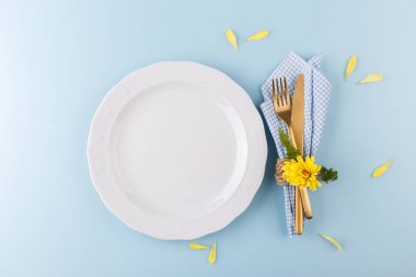 Altın çatal bıçak takımlı bahar ya da Paskalya sofrası. Mavi masa üzerinde sarı papatya çiçeği. Üst manzara.