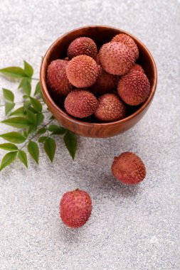 Ripe healthy lychee fruit in a wooden bowl on grey stone background with copy space clipart
