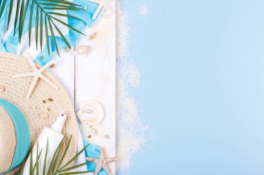 Mavi arka planda plaj aksesuarları, güneş gözlüğü, güneş kremi, parmak arası terlik, havlu ve şapka, yaz tatili konsepti, fotokopi alanı