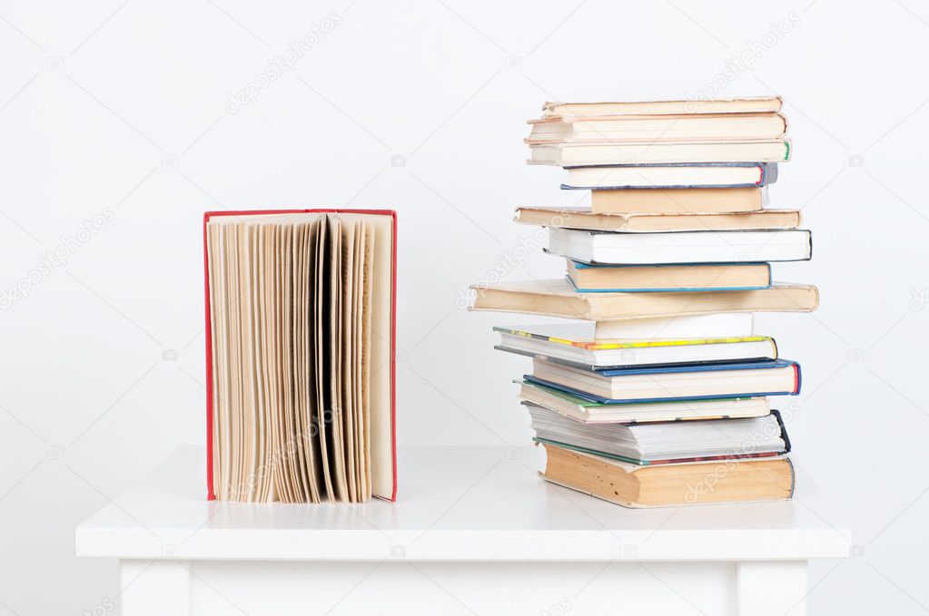 Stack of hardback books and old open book on white wall background. Search for relevant necessary information.