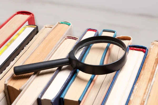 Büyüteç ile eski ciltli kitap yığını. İlgili ve gerekli bilgileri arama.