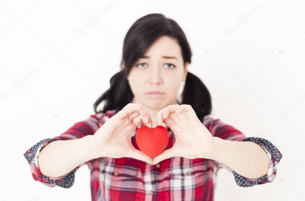 Sad young girl holding a small red heart and her fingers in the