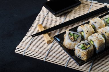 Uramaki suşi bambu peçete üzerinde siyah plaka üzerinde 