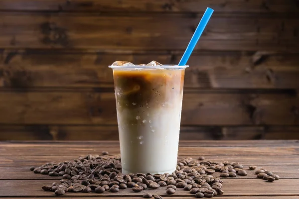 Ice coffee in takeaway cup and coffee beans on wooden background