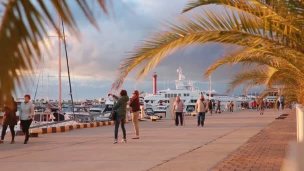 Άνθρωποι περπατούν κατά μήκος ενός μετώπου στο λιμάνι του Σότσι, ηλιοβασίλεμα, ήρεμη θάλασσα, Ρωσία — Αρχείο Βίντεο