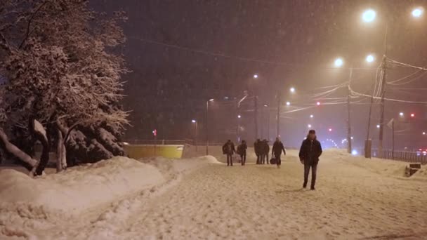 Os pedestres apressam-se ao longo da calçada sob queda de neve anormal à noite — Vídeo de Stock