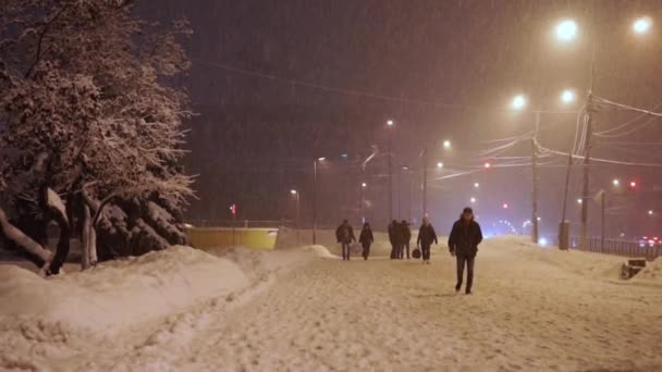 Os pedestres apressam-se ao longo da calçada sob queda de neve anormal à noite, câmera lenta — Vídeo de Stock