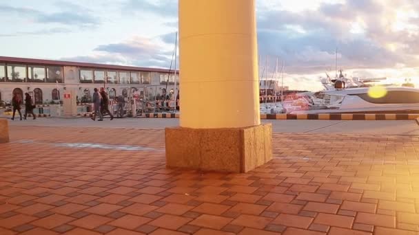 La gente está caminando a lo largo de un frente en el puerto de Sochi, puesta de sol, mar tranquilo, Rusia — Vídeo de stock