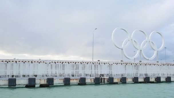 Anillos olímpicos en el puerto marítimo de Sochi, luz del atardecer, mar tranquilo — Vídeo de stock