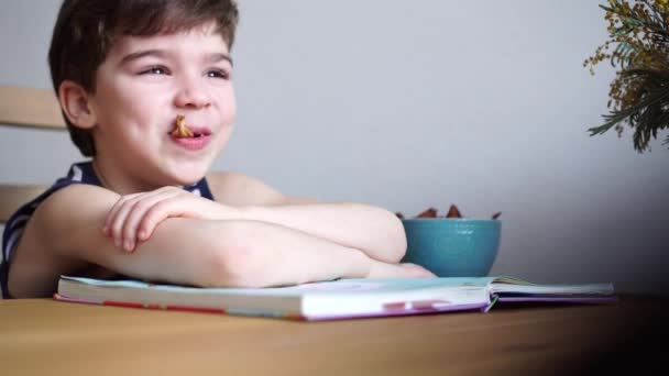 Encantador niño de 6 años echando a perder después de leer el libro y comer frutos secos — Vídeos de Stock