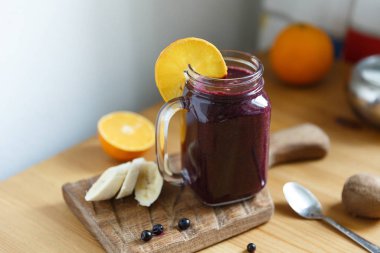 Mason kavanozu fincanı, içinde kuşüzümü, yaban mersini ve muz olan sağlıklı meyve suyu dolu.