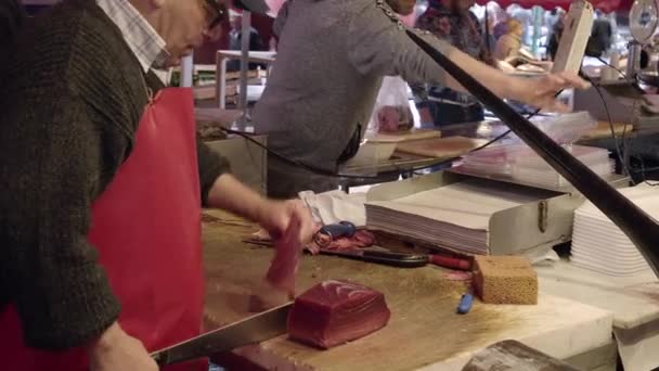 Продавец в красном фартуке отбивает рыбу-меч большим ножом, кладет его на прилавок — стоковое видео