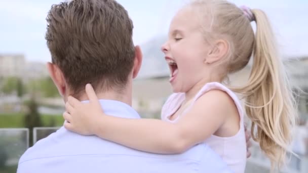 Vader van middelbare leeftijd omarmt zijn dochter. Klein meisje met blond haar glimlacht gelukkig — Stockvideo