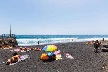 Tipik tenerife plajı. Siyah volkanik kum, güneş banyosu ve yüzen insanlar.