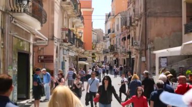 Sicilya 'da küçük Taormina kasabasının kalabalık güneşli caddesinde insanlar.