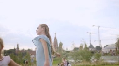 Mavi ve gül rengi elbiseli iki sevimli uzun saçlı kız kardeş çayırda dans ediyor.