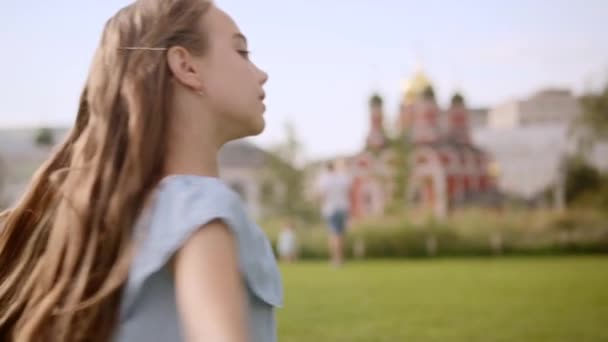 Charmantes langhaariges Mädchen in einem blauen Kleid dreht sich im Sommer in einem Stadtpark beim Tanz — Stockvideo