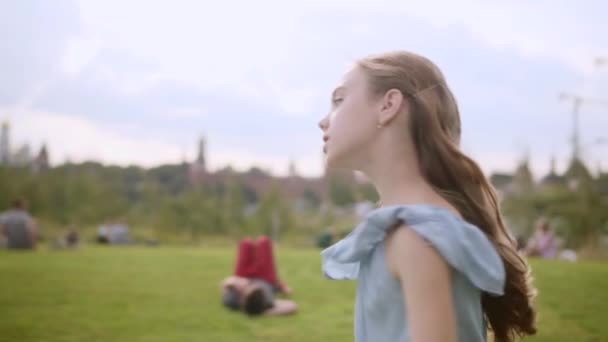 Encantadora menina de cabelos longos em um vestido azul girar em dança em um parque da cidade no verão — Vídeo de Stock