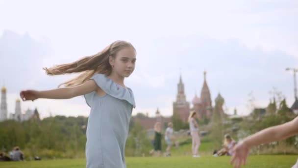 Két imádnivaló, hosszú hajú nővér kék ruhában és rózsaruha táncol a réten. — Stock videók