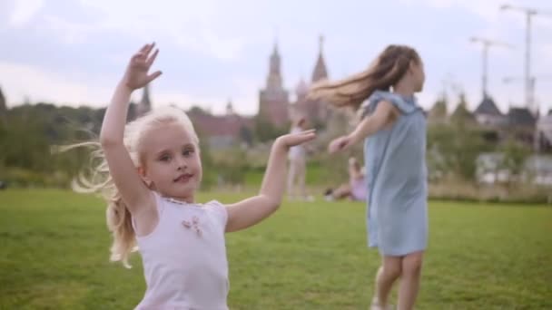 Két imádnivaló, hosszú hajú nővér kék ruhában és rózsaruha táncol a réten. — Stock videók