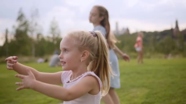 Due adorabili sorelle dai capelli lunghi in abiti blu e rosa che danzano sul prato — Video Stock