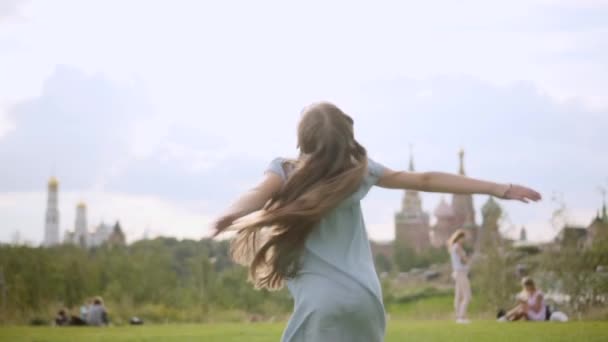 Elbűvölő hosszú hajú lány egy kék ruha spin tánc egy városi parkban nyáron — Stock videók