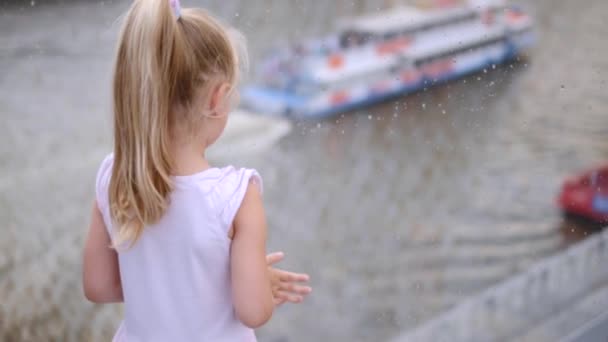 Klein meisje in roze kijken naar rivier en schip door glazen brug, slow motion — Stockvideo