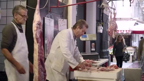 A butchershop. Meat carcasses hunged on hooks. butcher chopping meat, wrapping it in paper — Stock Video