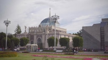 İnsanlar VDNH parkında yürüyor. Pavyon 11 Kazakistan, çiçek tarhı, yaz bulutlu bir gün.