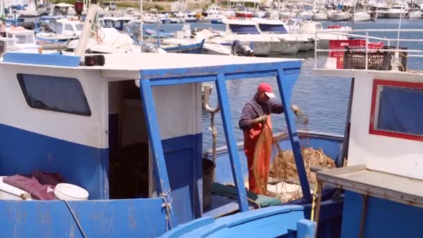 Debonair рыбак распутывает сеть, стоя на рыбацкой лодке в порту — стоковое видео